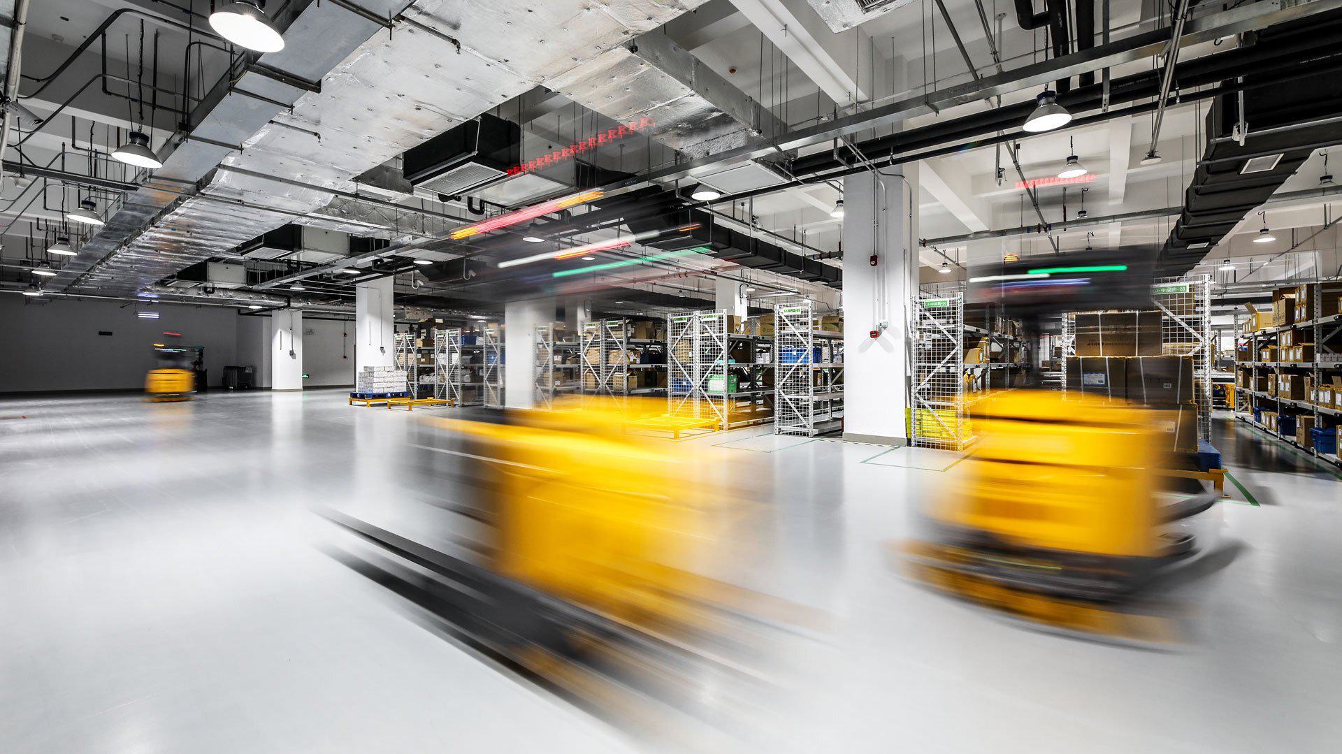A modern warehouse with yellow trucks moving quickly along the floor, creating a motion blur effect.