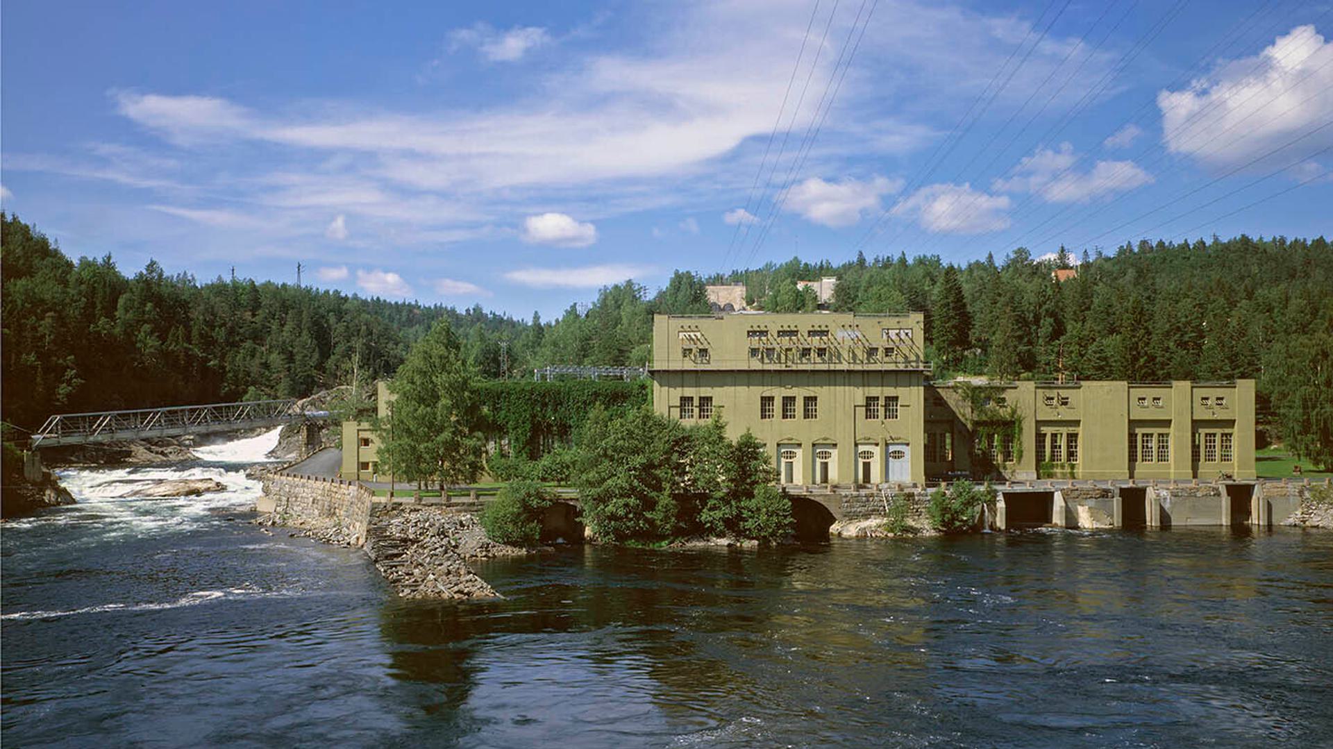 The Bøylefoss power plant, located by the river surrounded by lush green trees and a clear blue sky.