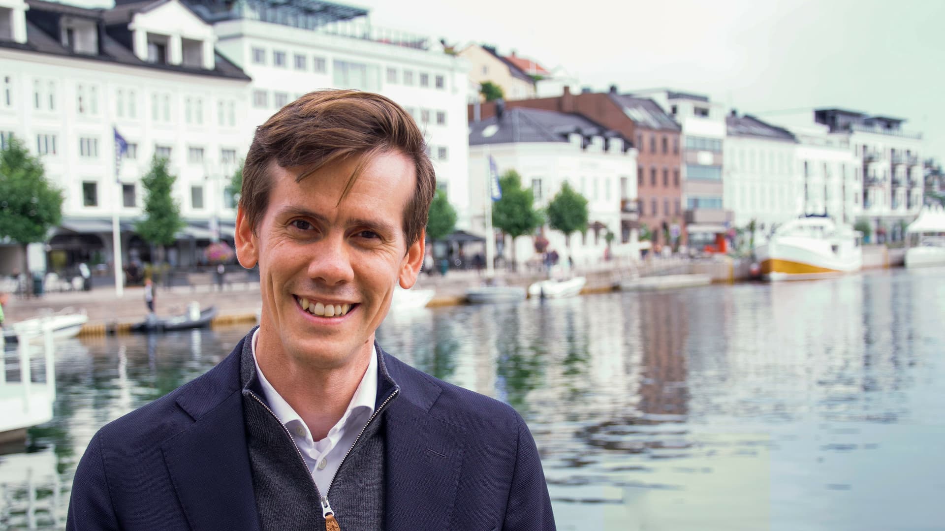 Portrait photo of CEO Benjamin Golding in front of the office building at Pollen, Arendal. With the ocean and boats in the background.