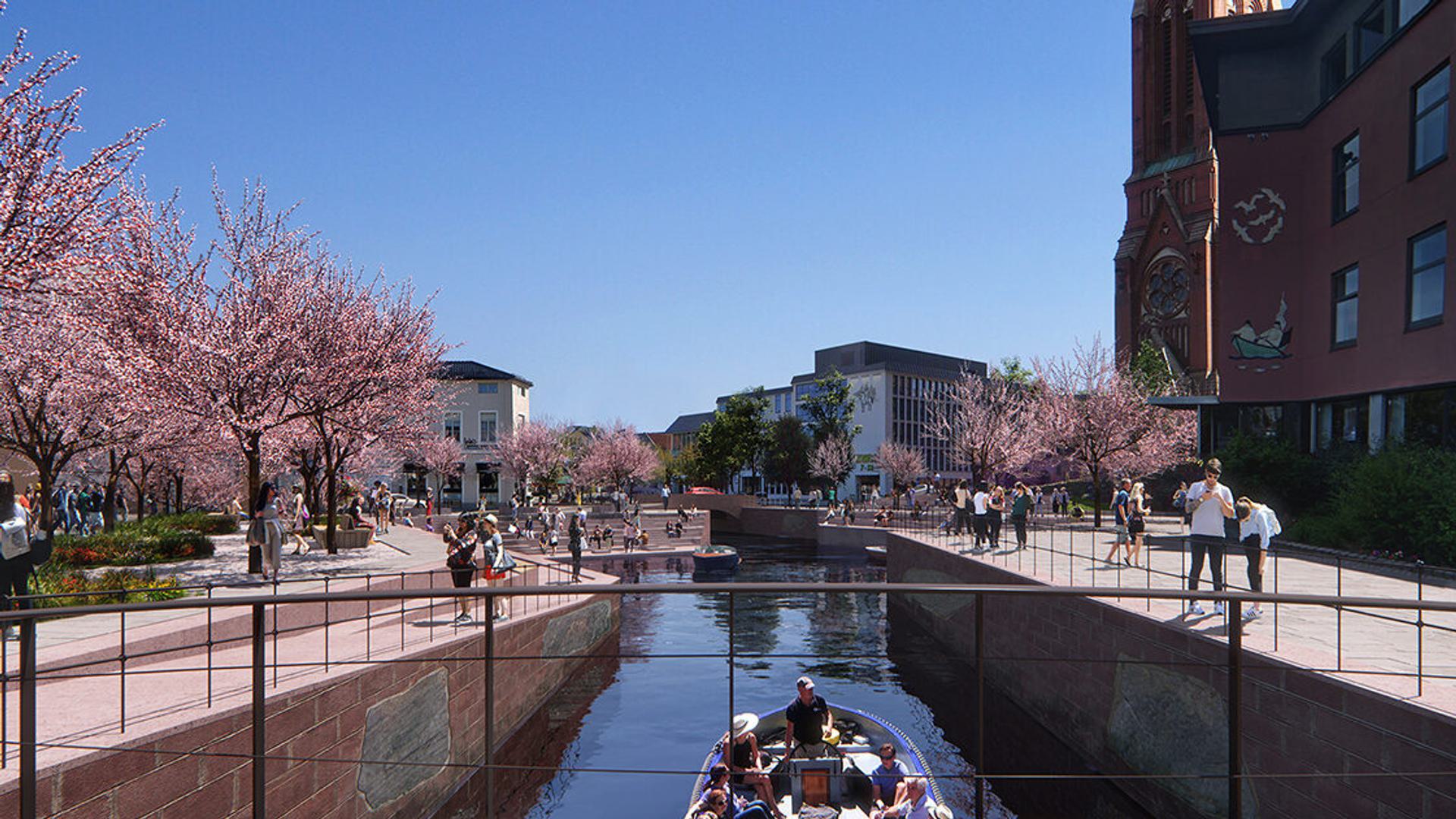 Photo of Snohetta canal in Arendal with people enjoying a sunny day along a canal. Cherry blossom trees in full bloom line the walkway, adding a splash of pink to the scene.