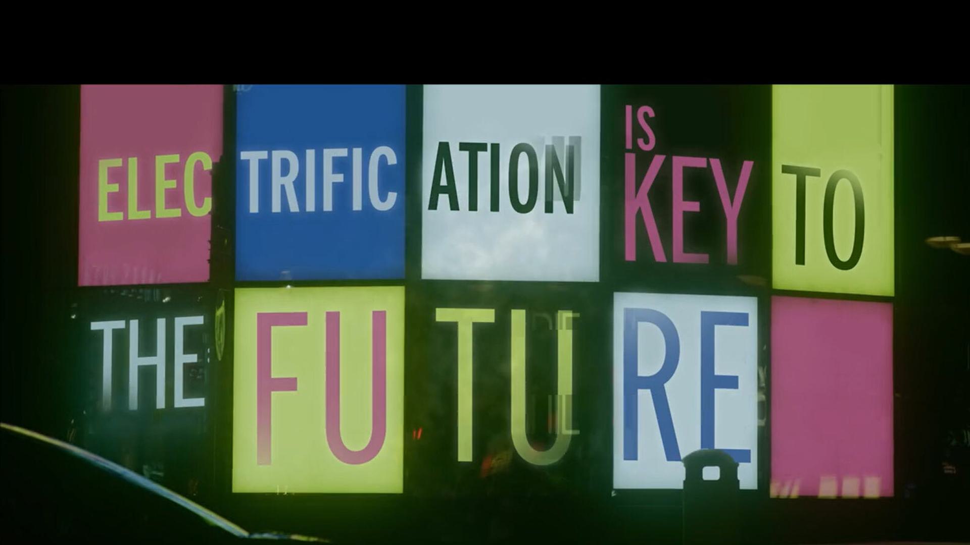 A brightly lit sign with a colorful grid design displaying the text "ELECTRIFICATION IS KEY TO THE FUTURE." The words are divided into individual sections with varied backgrounds in shades of pink, blue, green, and white, creating a vibrant and eye-catching effect.